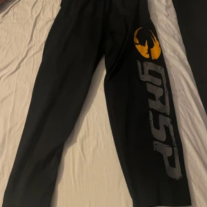 Svarta gasp mesh byxor - Snygga svarta träningsbyxor med ett coolt tryck i gult och grått längs benet. Perfekta för gymmet. Byxorna har en elastisk midja för extra komfort.