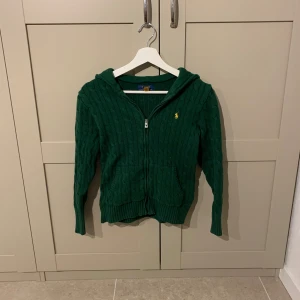 Grön zip Hoodie från polo Ralph lauren - Fin kabelstickad zip hoodie från polo Ralph lauren i mycket bra skick och med en fin mörkgrön färg. Nypris 1800kr. Köpt 2024.