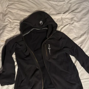 Svart sail racing hoodie - Svart hoodie från sail racing. Perfekt för både sommar och vinter. Den har en smidig ficka vid bröstet.