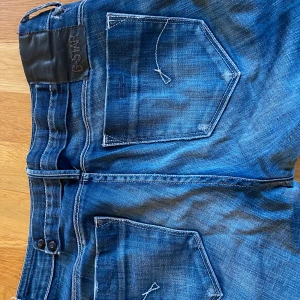 Blå jeans från G-Star RAW - Snygga blå jeans från G-Star RAW med en klassisk femficksdesign och tydliga sömmar. Jeansen har en knappgylf och en lätt tvättad look som ger en cool stil. Perfekta för en avslappnad vardagslook. Pris kan diskuteras.