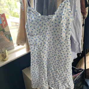 Blommig klänning - Perfekt midsommarklänning med mönster av små ljusblå blommor. Knytning på axlarna. Passar S/M. Använd en gång, bra skick.