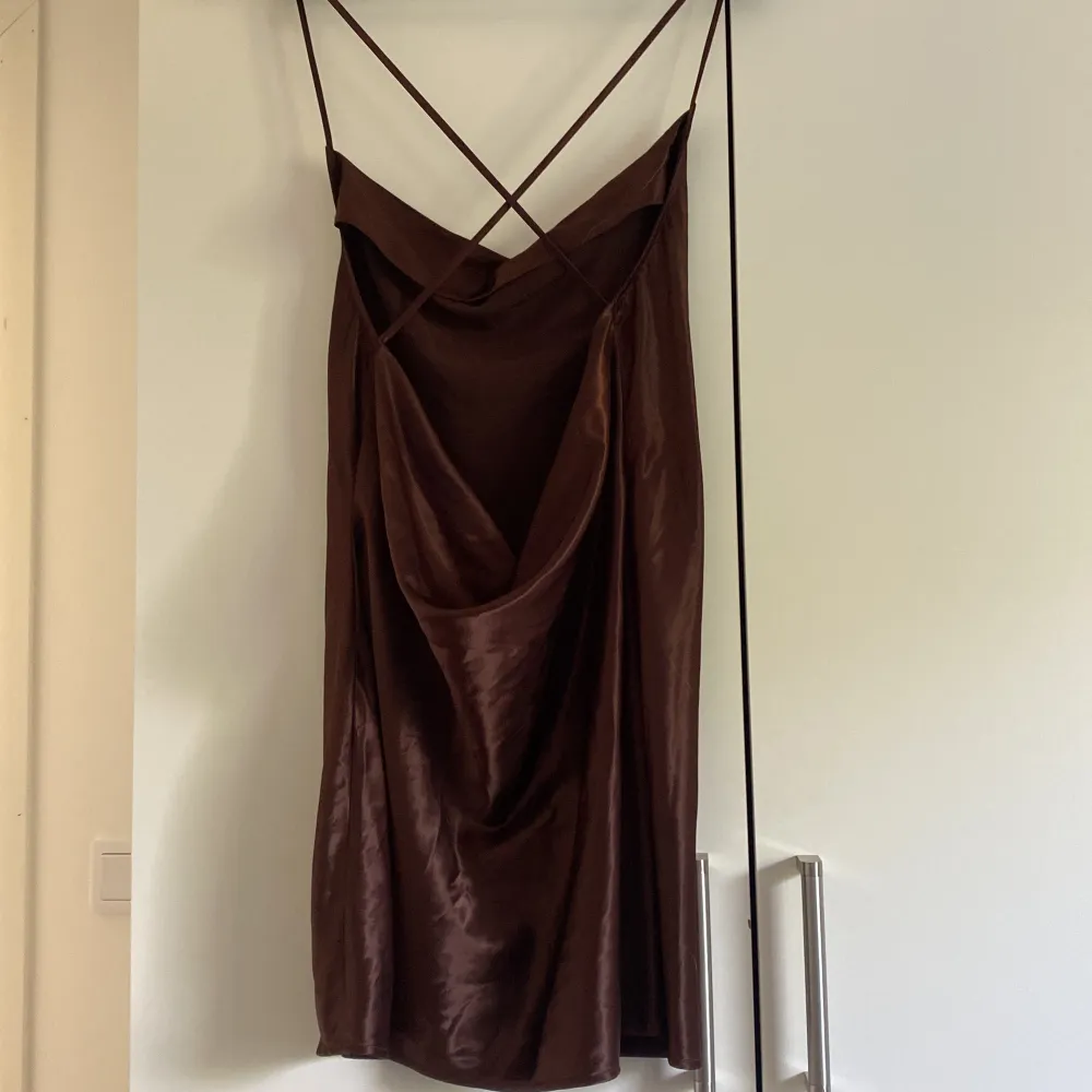 En brun klänning i glansigt matreal  som är korsad och lägre i ryggen . Klänningar.