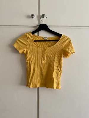 Gul somrig t-shirt - Sommarens bästa t-shirt! Ribbad med knäppning längst hela framsidan. BabyT känsla, något croppad 