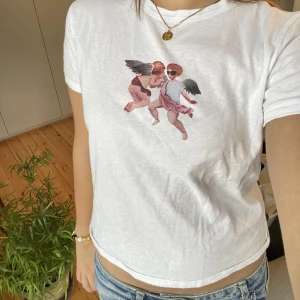 Vit tröja med änglar - Säljer en vit croppad tröja med änglar tryck från zara. Den har andvänds ett få antal gånger och är i väldigt bra skick.