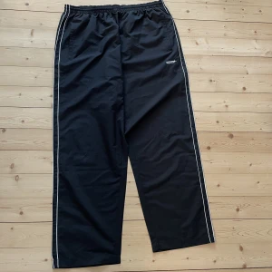 Oversize träningsbyxor - Mycket luftiga, svarta träningsbyxor med vita revärer på sidorna. Köpta på second hand, troligtvis helt oanvända då originalprislappen sitter kvar. I storlek XXXL, men går att stylea (se bild). 