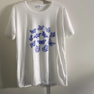 T-shirt  - Vit T-shirt med blåa fjärilar. Oanvänd och lent material. Står M men passar också S