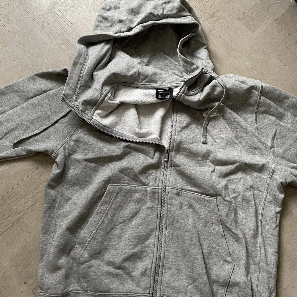 En grå nike zip hoodie med vit logga. Hoodien är i bra skick och storlek M tts. Priset kan justeras.🙌. Hoodies.