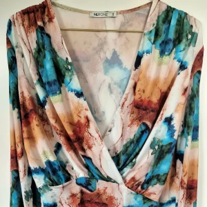 Balloon Sleeve Bodysuit - OANVÄND!  Mönstrad body från NLY One. Omlottlagd v-ringning framtill. Ballongärm med resår i ärmslut. Stretchigt och slätt material med lyster. Lagda veck över axlar. Stringmodell med tryckknappar i gren. 