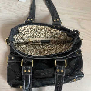 Skit snygg lack väska!! - Super fin lack väska med leopard print, som rymmer massor! Lacket håller däremot på att lossna på både axelbanden och ”sidorna” och därför blir det som små svarta korn efter väskan. Det finns ett annat axelband i väskan om man vill ha det istället <3 