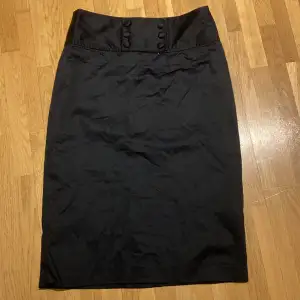 Svart rak kjol 63 cm Dekorknappar fram och dragkedja bak 