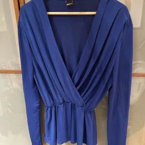 Gina tricot m l blå topp med volang  - Snygg topp från Gina Tricot med djup omlott v-ringning och resår i midjan. Ganska stor i stlk o passar även L bra. Fint skick! 