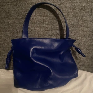 Väska - Klarblå väska från ginatricot, aldrig använd! Perfekt mellanstorlek som passar till alla tillfällen, justerbar upptill med hjälp av banden på sidorna.