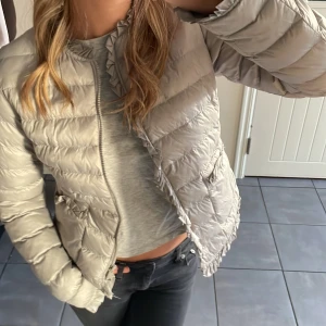 Grå dunjacka - Supersöt grå dunjacka, med som små volanger som sömmar, två fickor vid sidorna, använd fåtal gånger, bra skick!🥰den är i storlek m men passar mig som vanligtvis bär s