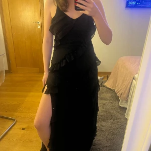 Svart klänning  - Säljer min svarta långklänning med volanger och lågrygg, klippt och sytt egen slitts i den även sytt upp den till mig som är 160cm