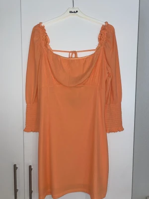 Peachfärgad kortklänning  - En orange klänning i pliserat material, med en väldigt vacker öppen rygg🌼