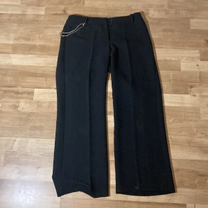 Svarta kostymbyxor  - Svarta kostymbyxor med en liten kedja med typ kristaller, har gått sönder lite vid knapparna men går bra att använda tycker jag