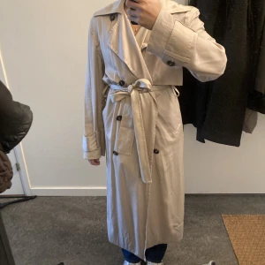 Beige trenchcoat - Beige trenchcoat från Weekday.  strl XS, oversize. Tunn, passar på sommaren/våren. I fint skick, använd ca 5 gånger. Köpt 2022. Utsida: 100% lyocell Foder: 54% polyester 46% viskos