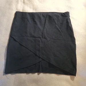 Svart minikjol med omlott - Svart minikjol med omlott. Saknar lapp men gissar på storlek S-M. Inneeband har lite lösa trådar (se bild) men inget som märks när kan har den på 💛 Använd men mycket kvar att ge!