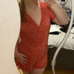 Byxdress från Pull&Bear - En röd byxdress från Pull&Bear med vita blommor på. Andvänd ca 2-3 ggr och är i storlek M