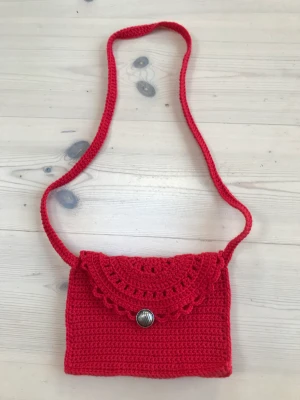 Virkad Röd kuvertväska  - Helt ny handgjord virkad väska. Spetsmönster på locket, stängs med en knapp. Lagom stor för mobil och något mer. Mått: 19x15 cm  Kan beställas i de flesta färger. Tar ca 1 v.  