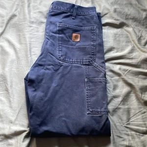 Carharrt arbetsbyxor  - Vintage carpenter byxor Carharrt i mörkblå. Har ett hål vid vänstra knäet samt lite färgstänk och annat på framsidan. Köpte dem redan använda. Storleken är lite mindre runt midjan än vad som står på byxan känns det som. Jag är ca 190cm lång. 