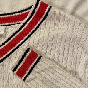 stickad tröja - Vit stickad trörja med V-neck och röda och blåa ränder. Tröjan är använd fåtal gånger men i bra skick. Sann till stor i storleken.