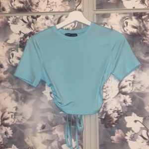 Kortärmad topp - Kortärmad ljusblå topp med knytning i ryggen, storlek s. Har en liten krage.  Aldrig använd. 