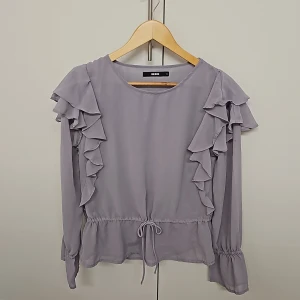 Blus - En fin blus med volanger som jag har haft på mig några gånger men är i bra skick. Vänster ärmen är tyvärr lite smutsig men det sysn inte mycket. Färgen är lite klurig då den upplevs som grå eller lila, men den är lila.