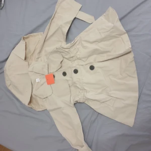 Flicka tranchcoat - Tranchcoat flicka. En lätta elegant jacka med knappar på framsidn och vid vristen. Luvan är avtagbar.  Smalare vid midjan ger en känsla av en klänning.  Aldrig använd. Etiketterna är på.  Storlek 90.