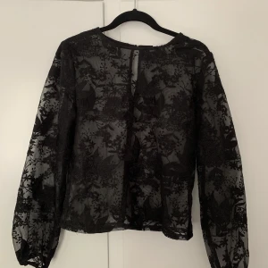 Topp - Genomskinlig topp med blommigt mönster. Har en knapp back i nacken. 