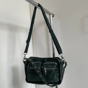 Cool mörkgrön väska - Cool mörkgrön väska💚 Två axelremmar, en kortare med nitar och en justerbar som även går att ta av. Supersnygg att ha både på axeln eller cross-body⭐️Just den mörkgröna färgen är ovanlig för modellen.