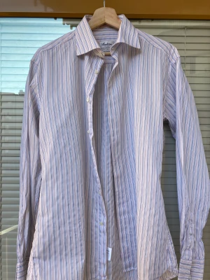 Randig Stenström skjorts - Säljer min flerfärgade randiga skjorta från Stenström då den heller inte längre används. Manchettknappar används för att stänga ärmen. Är i storlek 39 och i fitted body. 100 % bomull. Inköpt under hösten 2022. 