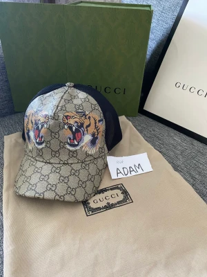 Gucci keps tiger med box - Mycket fin stilren Gucci keps av färgen beige samt tiger med prislapp och boxen med samt dustbag. Hör av dig vid intresse!