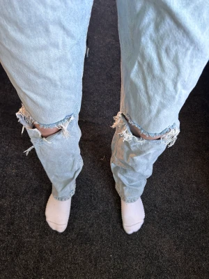 Gina Tricot jeans med hål - Gina Tricot, Jeans. Ljusblå med hål. Byxorna är inte strukna på bilden. Högmidjade. Knappen är inte grön, det är en reflektion. 