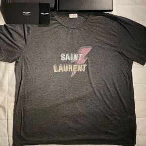 Saint Laurent T-shirt i Grå - Hej, säljer en väldigt bekväm T-shirt från Saint Laurent i 50% Polyester och 50% Viskos. Storlek Large men italiensk produktion så passar M. Utmärkt skick. Har låda, brev, tag från köp. Nypris runt 3500kr. Pris inte hugget i sten. Hör av er vid frågor!