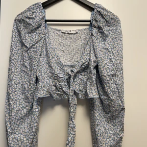 Blommig blus med volang NA-KD - Blus med volang och knytning fram.  Använd 1 gång, växte ur den lite för snabbt 😅 Nypris: 299:-