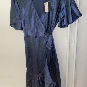 En helt ny festlig nattblå omlottklänning från Pieces. Storlek M, prislappen finns kvar. Materialen är glansigt satin. Originell pris 429,95SEK.