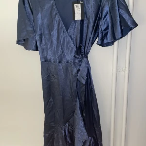 Ny Festlig omlottklänning - En helt ny festlig nattblå omlottklänning från Pieces. Storlek M, prislappen finns kvar. Materialen är glansigt satin. Originell pris 429,95SEK.