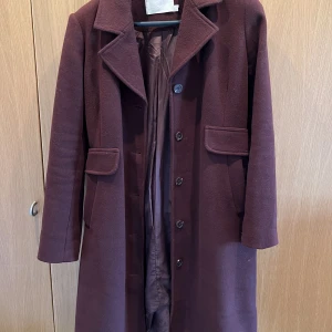 Kappa i bordeaux - Kappa One från Karen by Simonsen. Fast brett skärp i ryggen. Mörk vinröd typ Bordeaux. Sällan använd. Mått: Byst 58, längd 109.