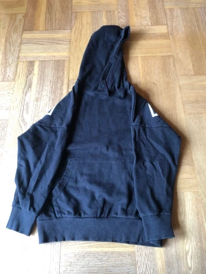 Luvtröja  - En svart luvtröja med vit text på ryggen. 