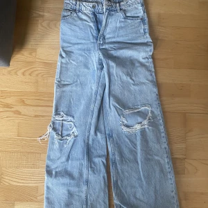 Ljusblå jeans  - Högmidjade ljusblå utsvängda jeans med hål på knäna. Från hm, divided. Hålen på knäna har lite lösa trådar men annars är jeansen i bra skick. Nypris 300kr.