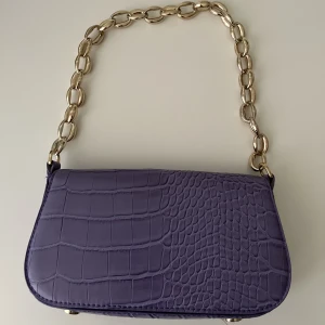 Lila axelväska från Zara - Axelväska från zara i färgen lila. Aldrig använd. Trots att väskan är liten får man plats med mycket i den. Aldrig använd.