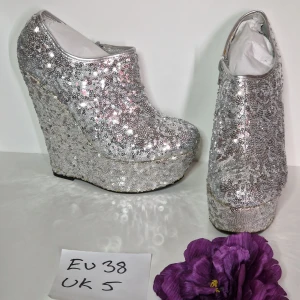 Kilklackar silver paljetter strl 38 - Silverfärgade kilklackar med hög klack Klackhöjd ca 15 cm Platå ca 5 cm Skorna är nya och oanvända men har fläckar, lim som blivit gult syns mer på bild än i verkligheten