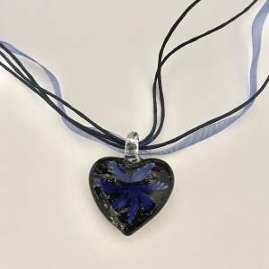 Blått halsband med ett hänge i glas i form av ett hjärta med en blomma i.