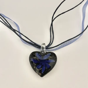 Halsband  - Blått halsband med ett hänge i glas i form av ett hjärta med en blomma i.