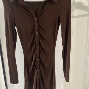Brun kroppsformad klänning - Denna bruna klänning är köpt på H&M och har ett ribbat material. Den har scrunch där framme som formar kroppen snyggt och går ner strax över knäna. Jättesnygg och har bra stretch. Den är XXS men kan passa någon med XS och S💗
