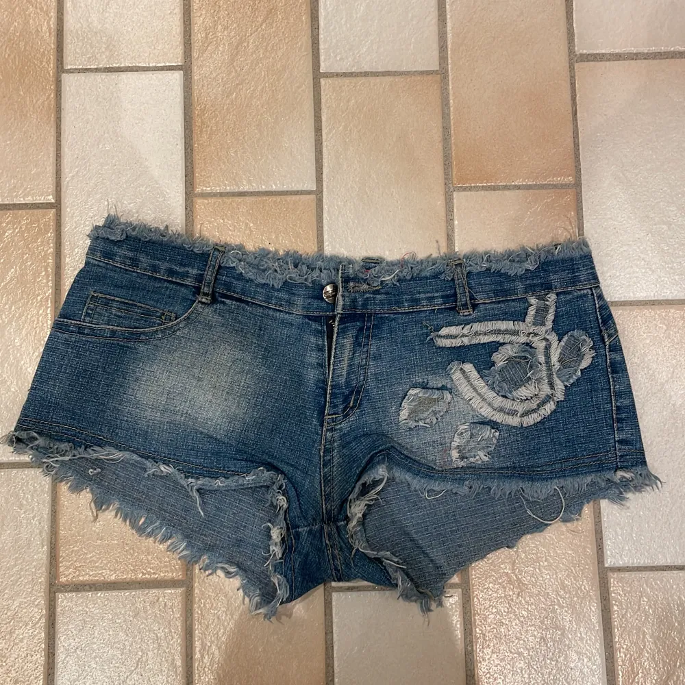 Söta jeans shorts med detaljer! Finns en fläck på vänstra sidan, se bild, men inget man tänker på och ska försöka få bort den! Midjemått 78cm shortsens längd 18cm. Shorts.