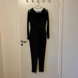 Byxdress - Svart figursydd byxdress i lyxigt material och virkade ärmar samt dekoltage. Använd endast 2 gånger