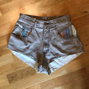 Vintage shorts från Bill Blass som passar runt storlek S. Brunbeiga med färgat mönster på fickorna och hög midja. 