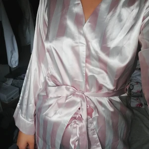  - Rosa/vit randig pyjamas-set i ett sidenliknande tyg. Överdelen har band i midjan och nederdelen har resår i midjan, båda delarna är helt nya och oanvända med lapp kvar. *laddar upp denna igen för att den förra annonsen försvann